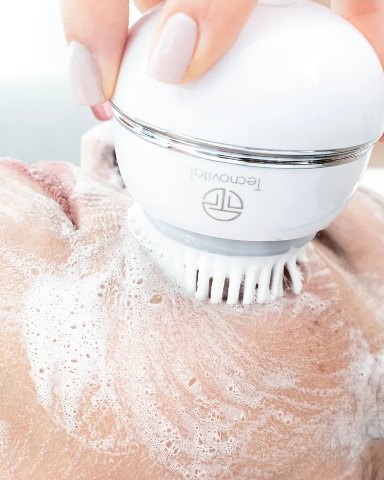Escova de limpeza facial deslizando sobre a espuma no rosto de uma cliente